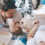 Couple eating pizza with their lovely dog on their bed in the bedroom.